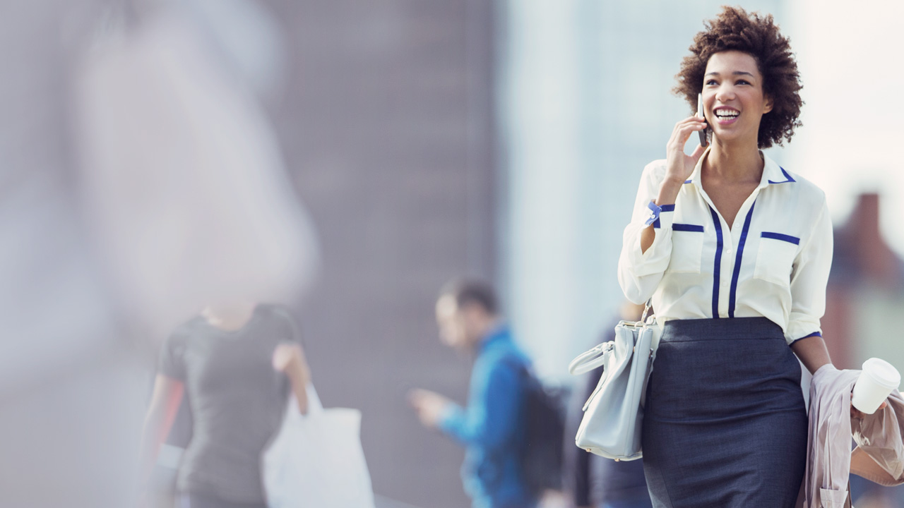 Woman outside smiling and walking while talking in mobile