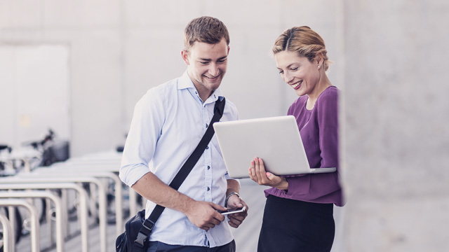 Two persons meeting outside an office are looking at a laptop