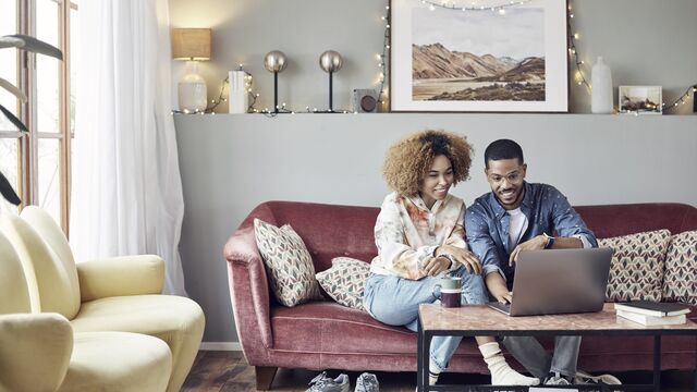 Smilende par hjemme som spiser og ser på laptop. 