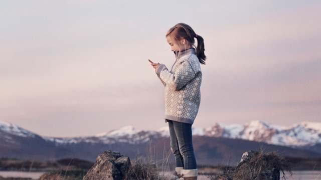 Liten jente står på en fjelltopp og ser på mobilen sin