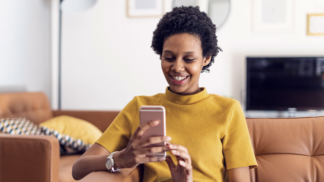 Smiling young woman at home using smartphone SMALL