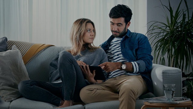 Et par som sitter i sofaen med laptop.