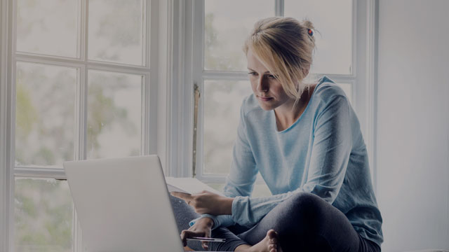 Ung kvinne sitter i vinduskarmen med laptop