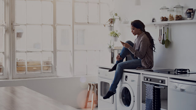 Ung kvinne som sitter på kjøkkenet oppå en vaskemaskin.