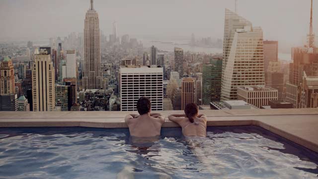 Et par som slapper av i utendørs basseng med utsikt over en storby. 