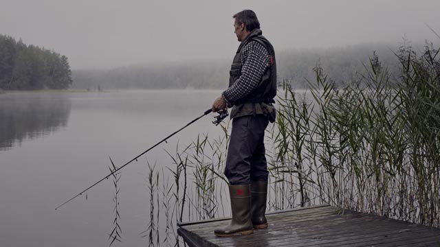 Eldre mann som står og fisker fra bryggekanten.