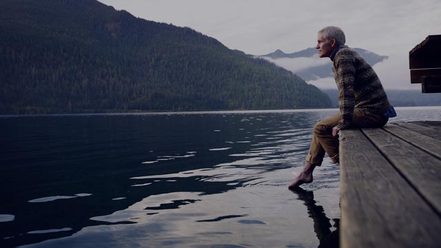 Eldre mann som sitter på bryggekanten og ser utover sjøen.