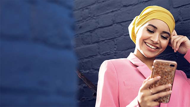 Girl smiling at phone by blue wall SMALL