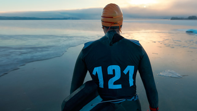 From behind you see swim runner man watching over frozen lake, winter landscape SMALL