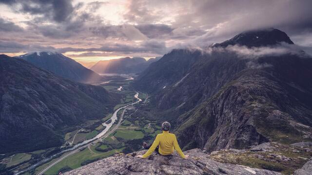 Mann på toppen av et fjell som ser utover et vakkert fjellandskap.