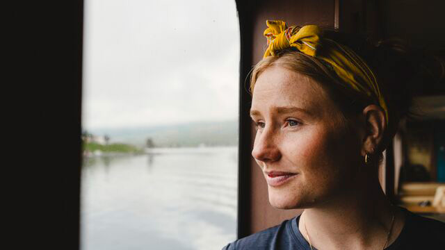 Yngre kvinne som ligger på stranden med sin mobil.