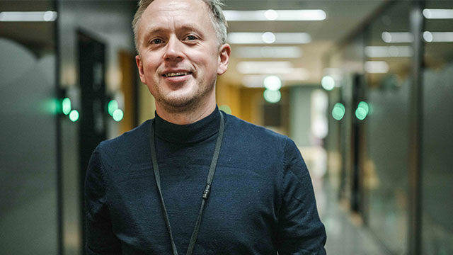 Anders Tveita smiler til kamera foran møterom
