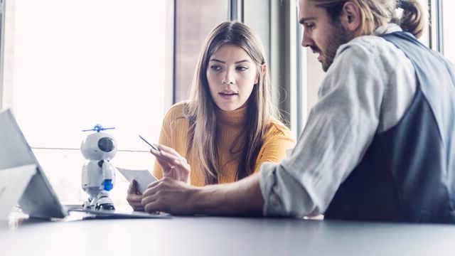 young-businesswoman-and-businessman-sitting-at-desk-in-office-talking-640x360