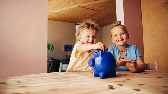 Two children putting coins in piggybank